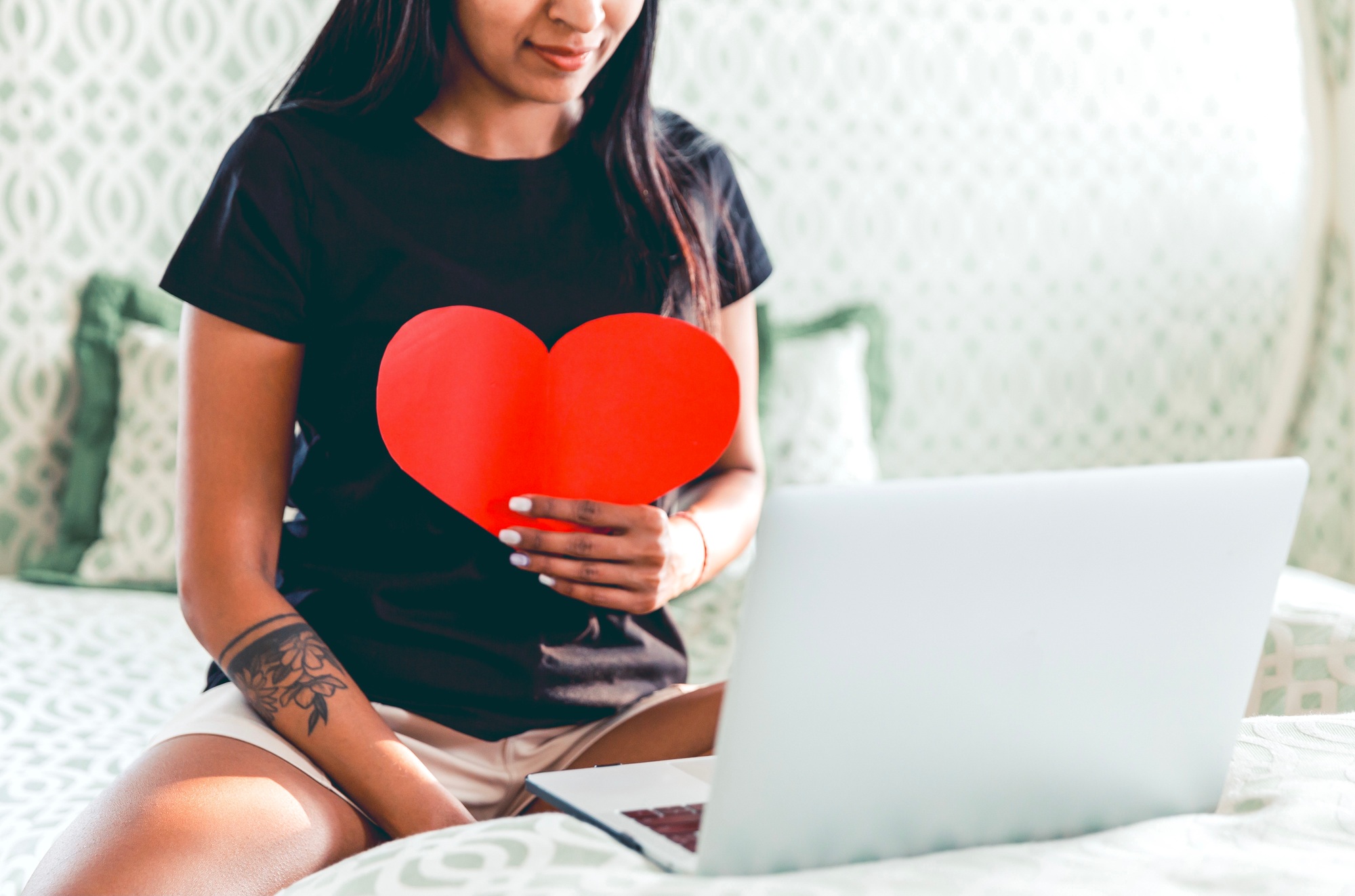 A woman smiling, chatting with lover, holding a heart, love during COVID, long distance relationship