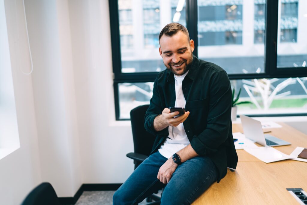 Cheerful man messaging on smartphone while sitting on table