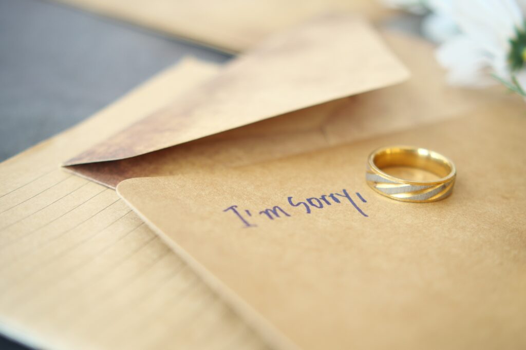 Note with the sorry word next to a wedding ring.